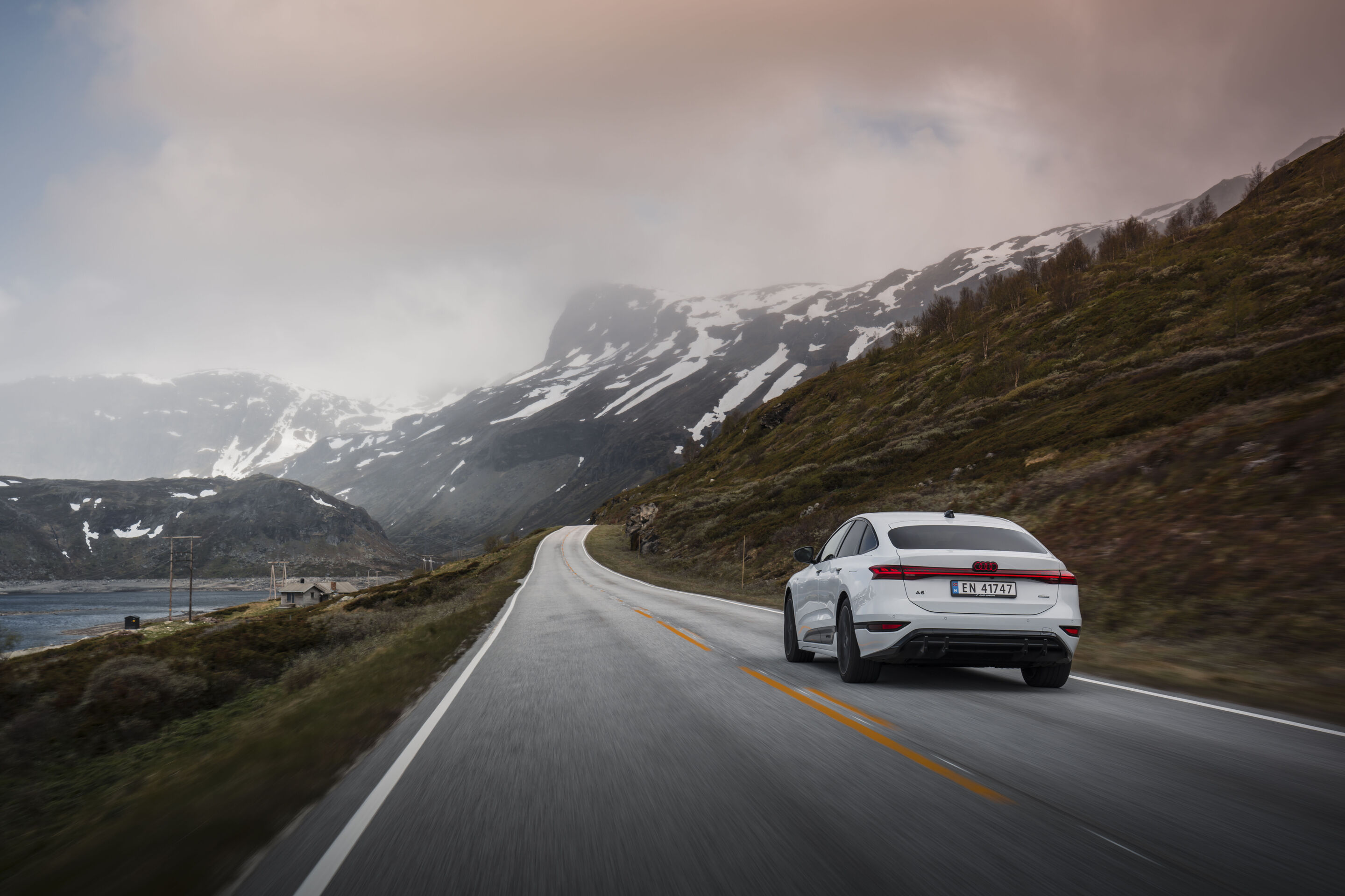 Buzul beyazı Audi A6 Sportback e-tron kar kaplı dağların önündeki yolda seyir halinde