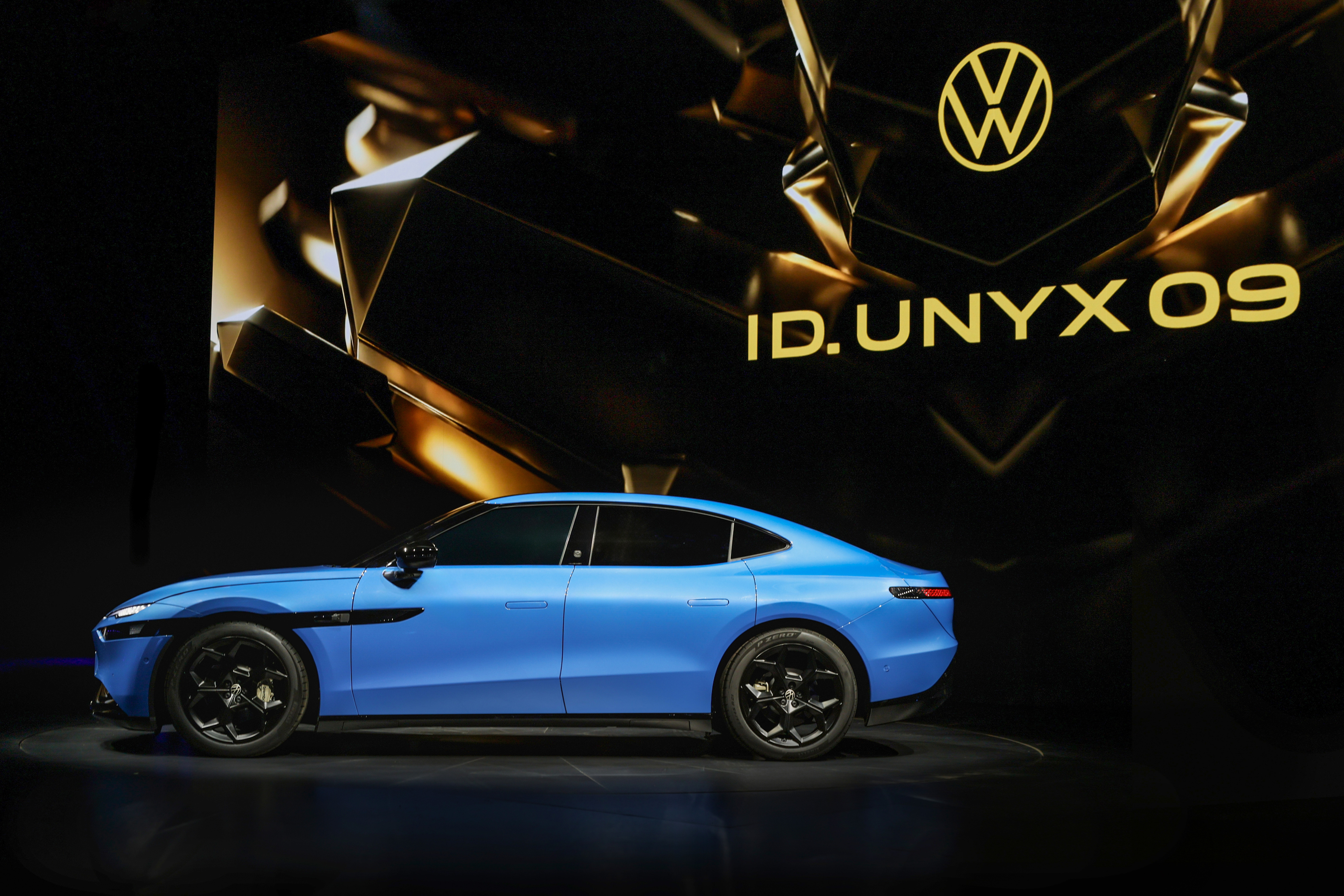 Volkswagen ID UNYX 09 sedanın siyah ve altın fon önünde yandan görünümü