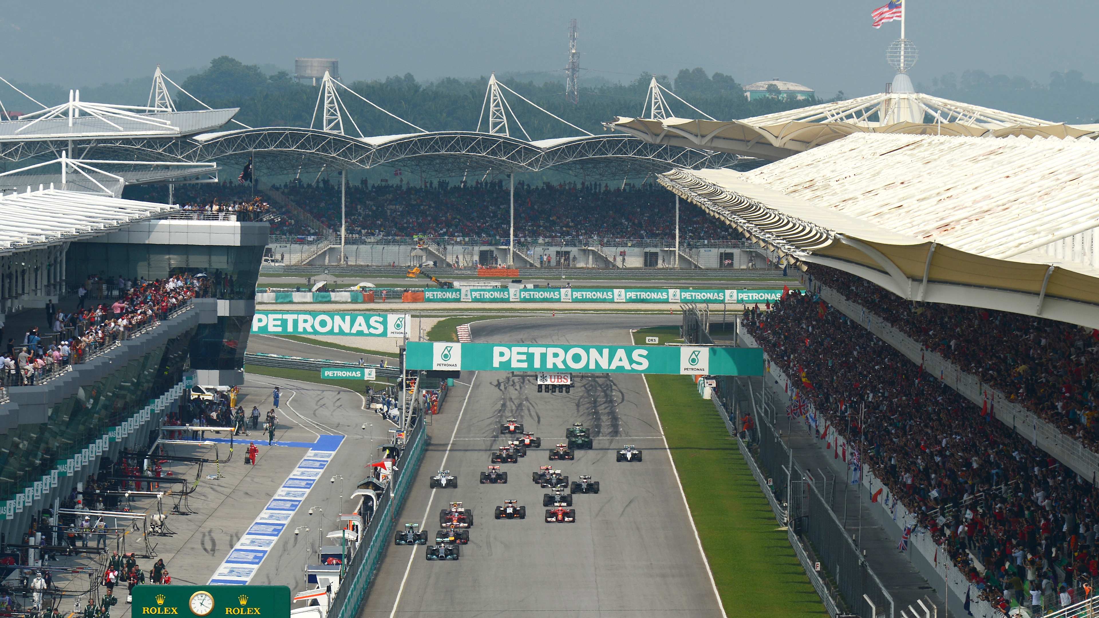 Sepang ana düzlüğünde sıralanmış Formula 1 otomobilleri ve dolu tribünler
