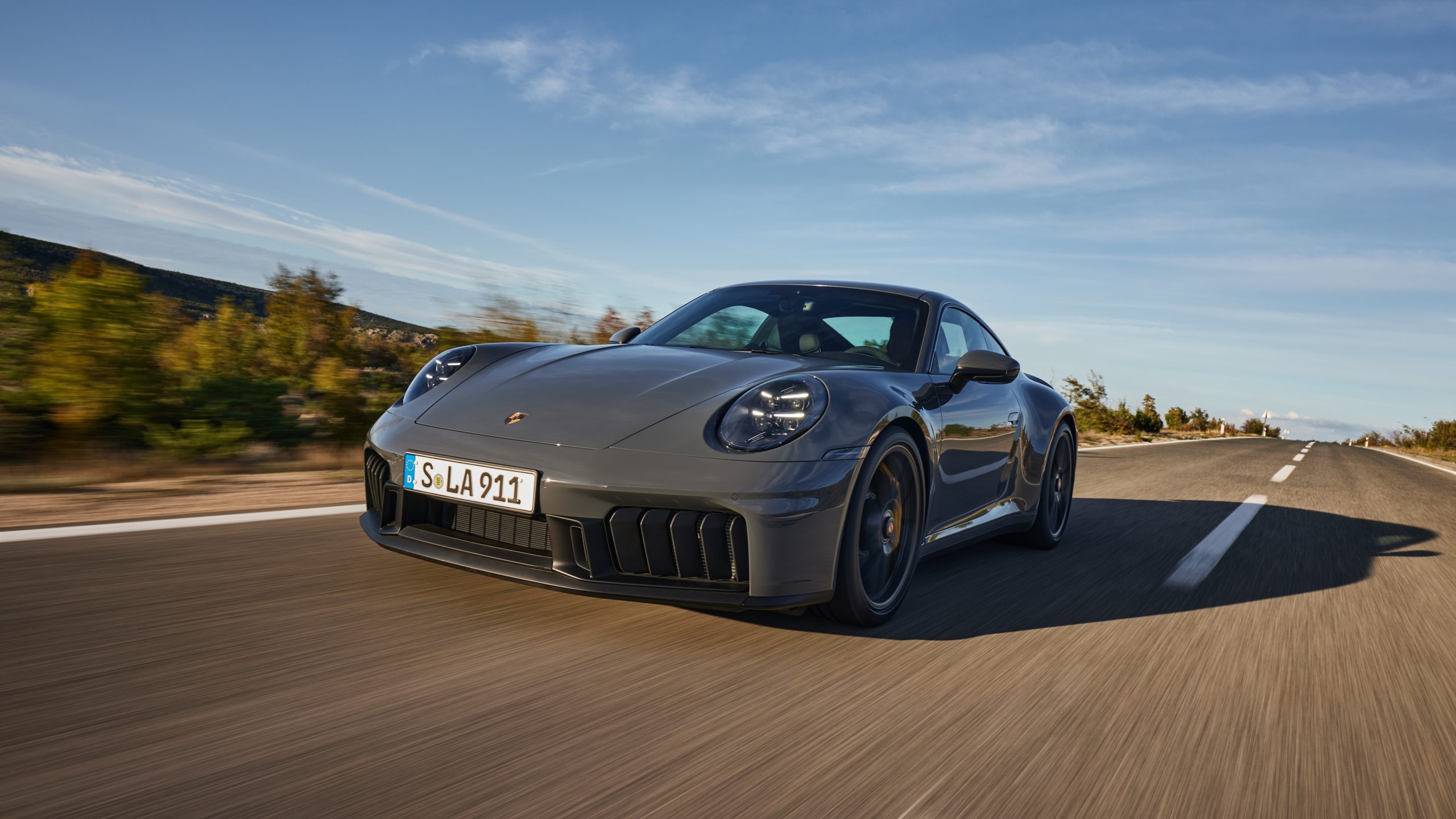 Gri renkli Porsche 911 Carrera GTS coupe açık yolda hareket hâlinde önden üç çeyrek görünümde
