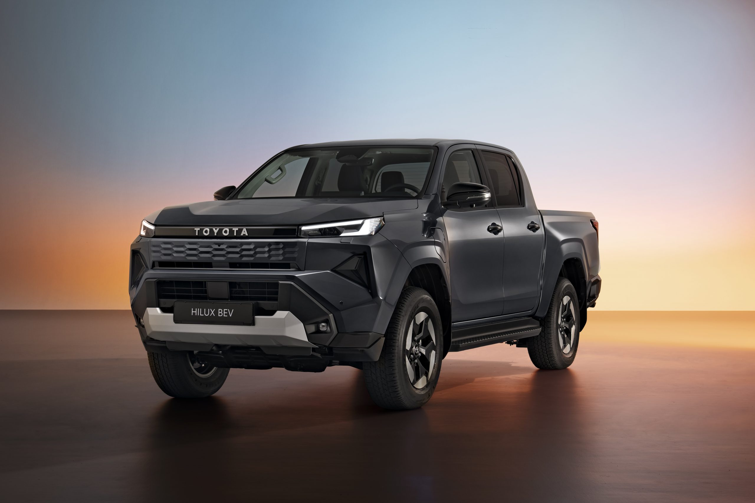 Koyu gri gövdeli Toyota Hilux BEV çift kabin pickup modelinin stüdyoda önden üç çeyrek görünümü