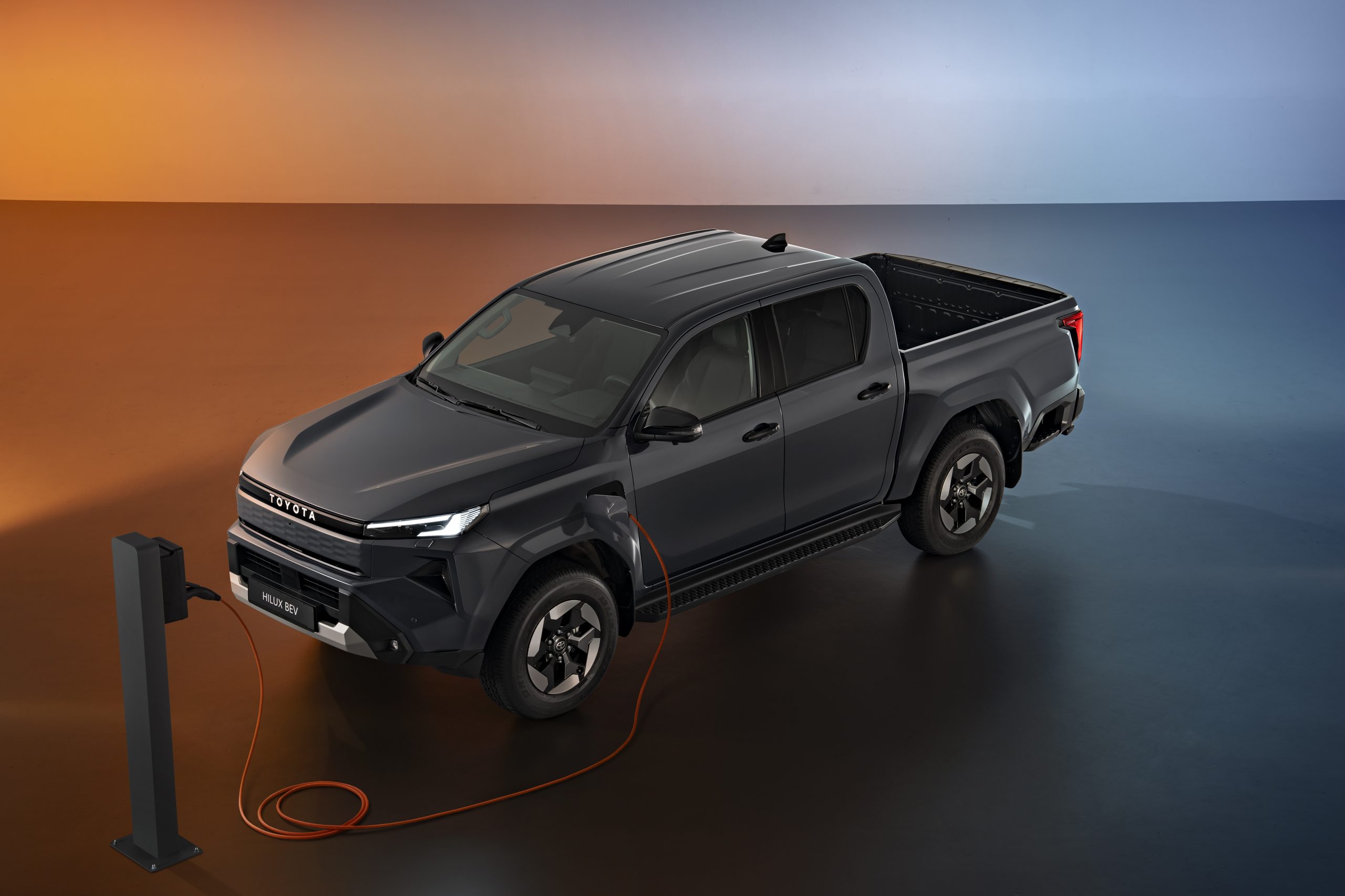 Şarj ünitesine turuncu kabloyla bağlanmış Toyota Hilux BEV pickup modelinin yukarıdan çekilmiş görünümü