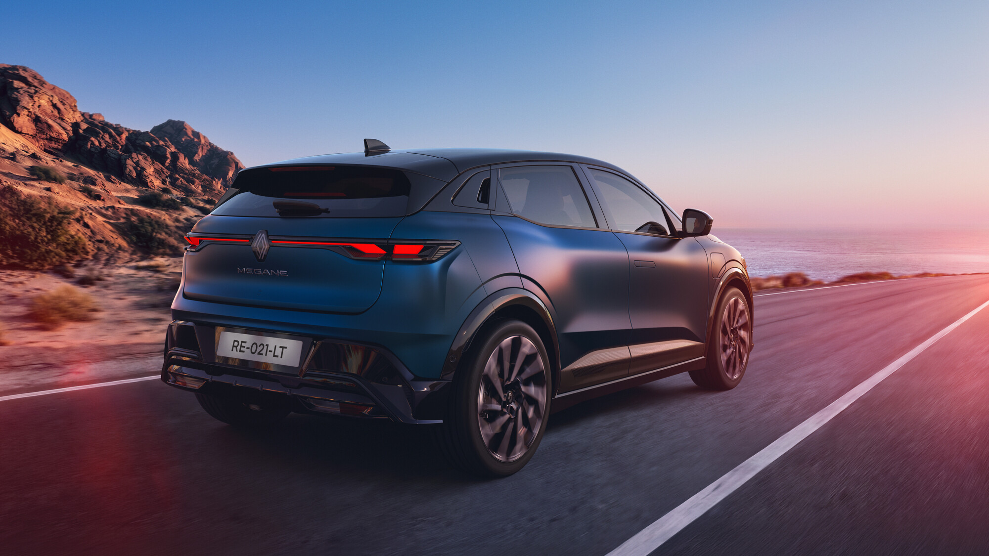 Mavi gövdeli Renault Megane E-Tech elektrikli modelin kıyı yolunda arkadan üç çeyrek görünümü