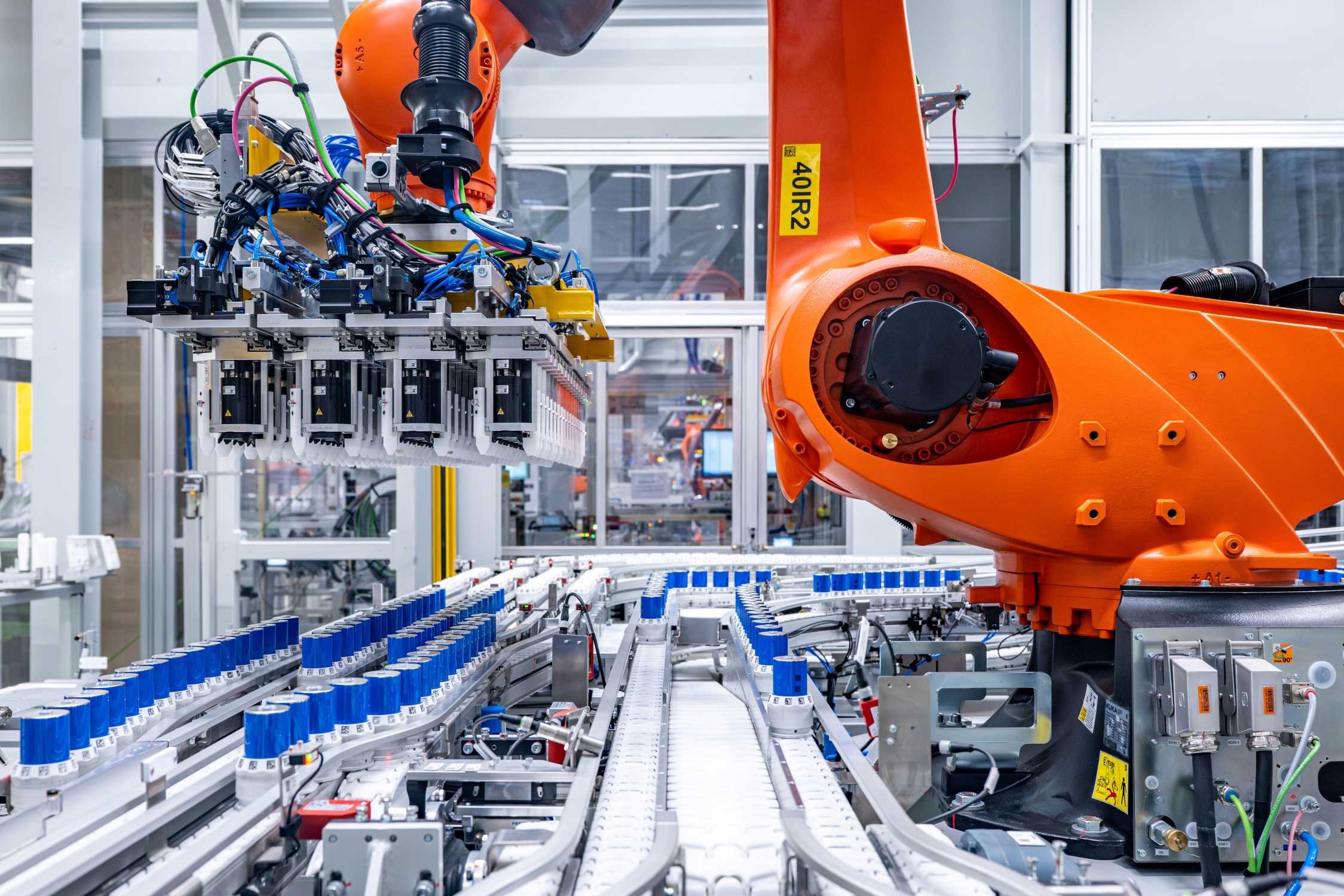 BMW Gen6 Batarya hattında silindirik hücreleri taşıyan turuncu robot kolu ve bant