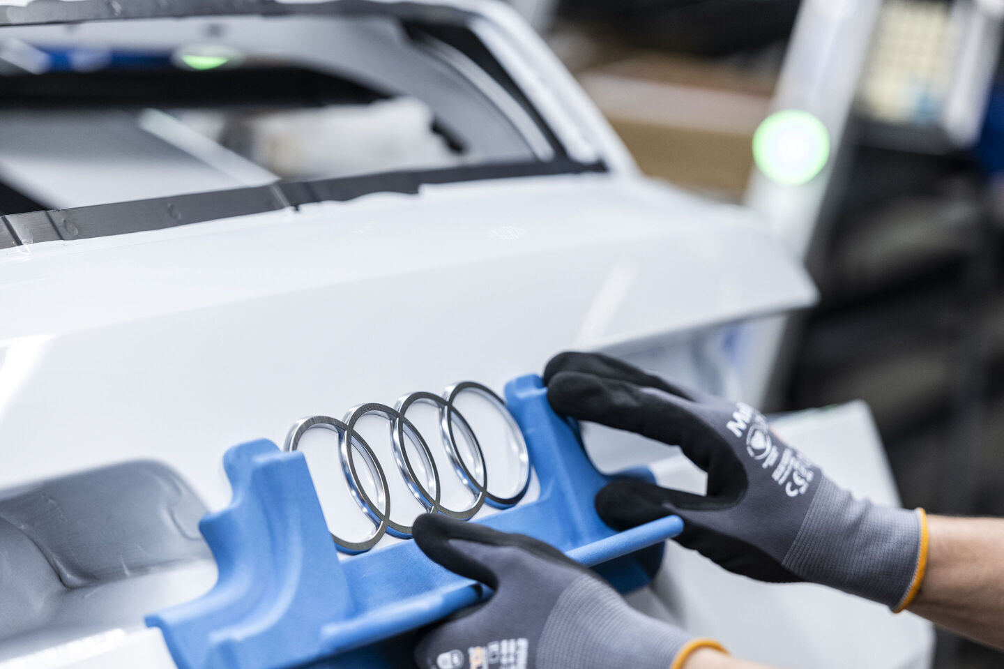 Audi A2 e-tron gövdesinde Audi halkalarını yerine yerleştiren eldivenli iki el, otomobilin arka kapağında montaj işlemi sırasında görülüyor
