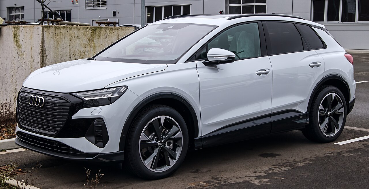 Beyaz renkli Audi Q4 e-tron SUV, ön ızgarası ve far tasarımı ile yoldan çekilmiş karede