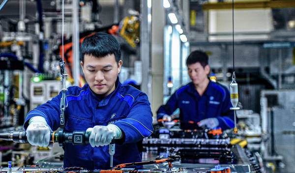 BMW Shenyang fabrikasında mavi iş tulumlu iki çalışan, Gen6 yüksek voltaj bataryası üzerinde tork aleti kullanarak montaj yapıyor