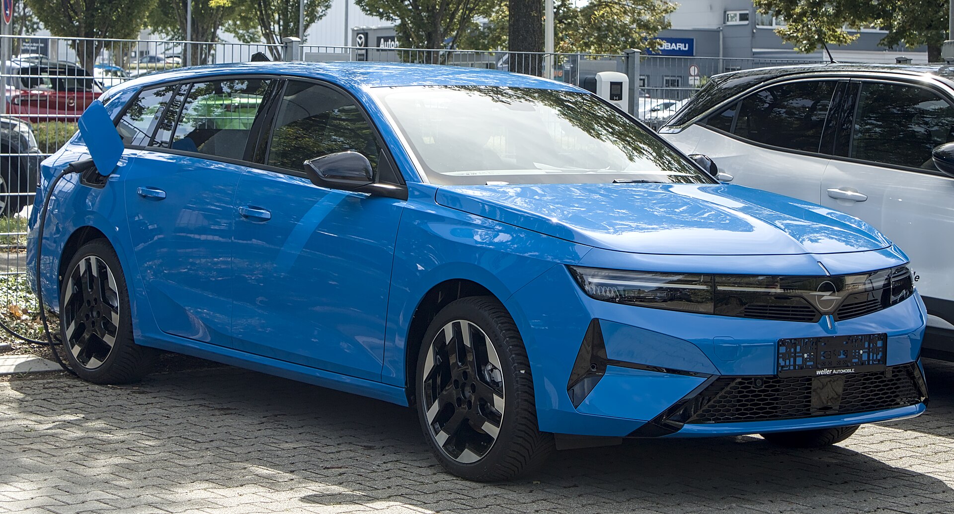 Mavi renkli Opel Astra Sports Tourer Electric, açık alanda yan ve ön profilden fotoğraflanmış