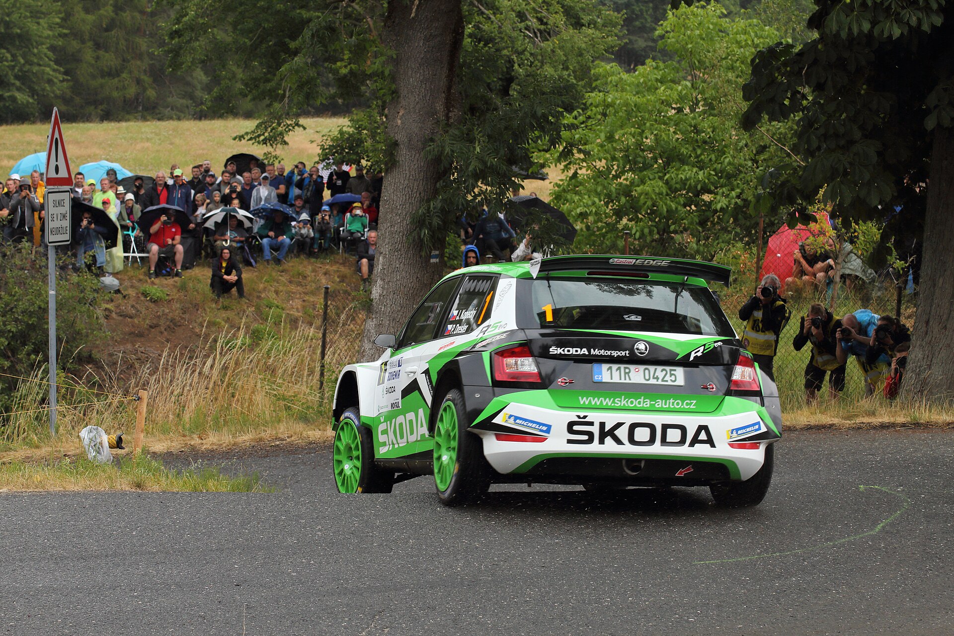 Seyircilerin önünde viraj alan yeşil beyaz Škoda Fabia R5 evo ralli otomobili