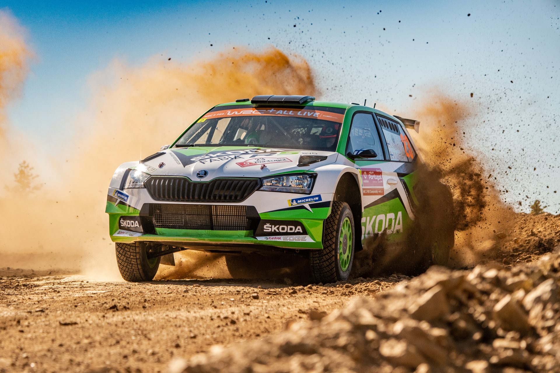 Toprak zeminde toz kaldırarak ilerleyen yeşil beyaz Škoda Fabia Rally2 evo ralli otomobili