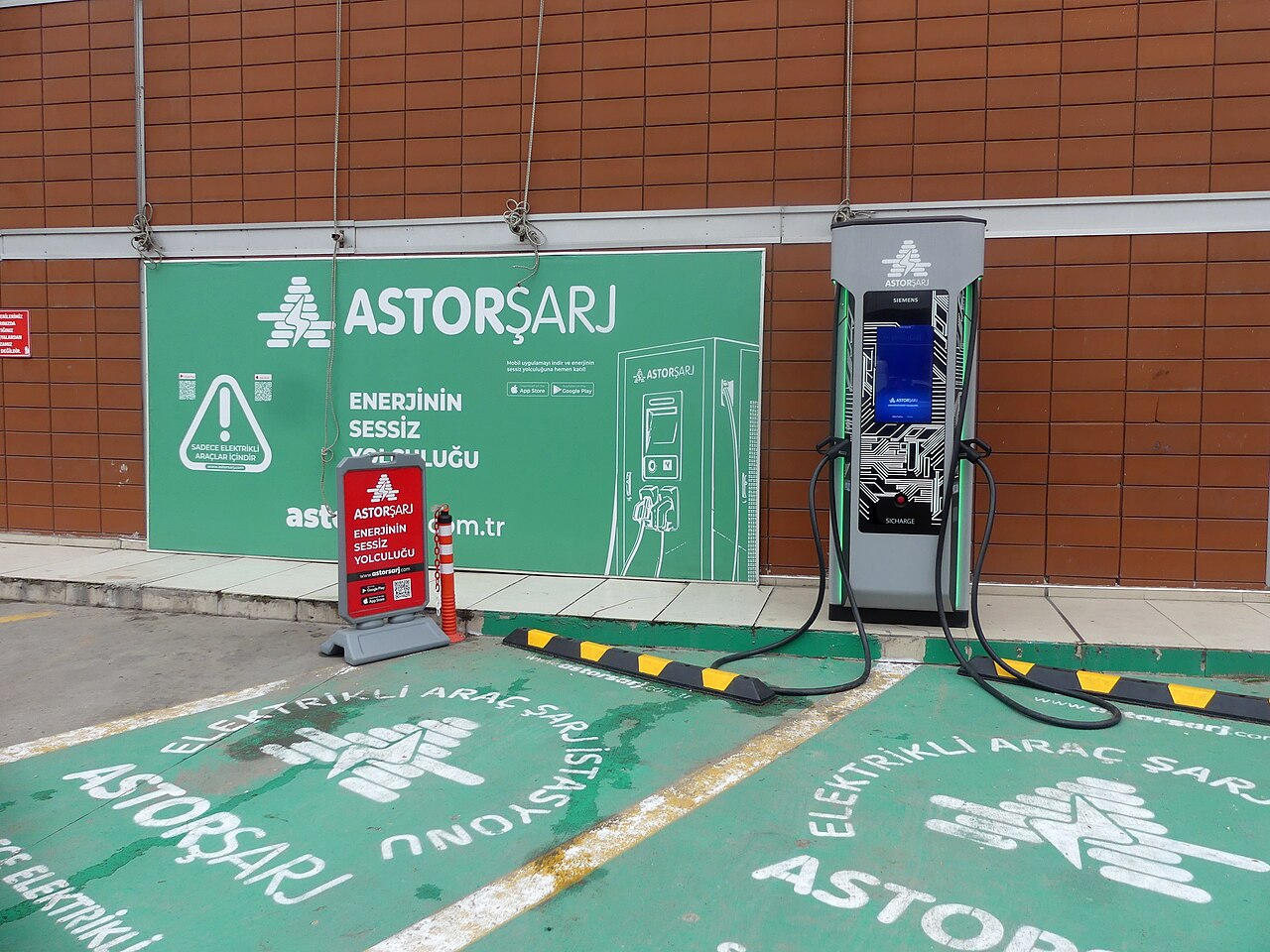 Türkiye'de bir alışveriş merkezi otoparkında Astor Şarj markalı hızlı şarj ünitesi ve yeşil boyalı şarj park yerleri