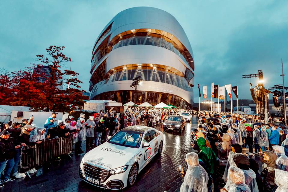 Yağmurluk giymiş kalabalığın arasından Mercedes-Benz Müzesi'ne ulaşan beyaz 140 yıl logolu S-Serisi